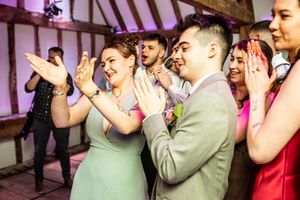 Wedding guests clapping and celebrating on the dance floor at a barn reception with purple lighting.