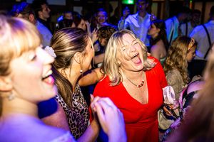 Joyful wedding guests dancing and laughing at an evening reception, woman in red dress smiling.