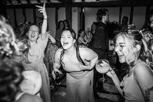 Guests dancing energetically on wedding reception dance floor in black and white photography at barn venue.