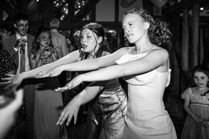 Two young girls strike a fun pose dancing together at wedding reception in black and white photo.
