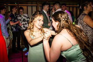 Two bridesmaids in sage green dresses laughing and dancing together at a wedding reception.