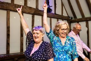 Two older women raising hands and dancing joyfully together at a wedding reception party.