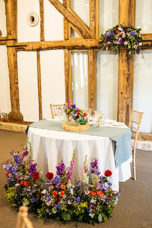 Elegant wedding sweetheart table decorated with colorful wildflowers in rustic timber-framed barn.
