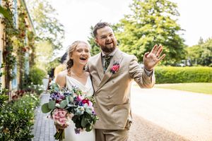 Happy bride and groom waving and laughing outdoors after their wedding ceremony.