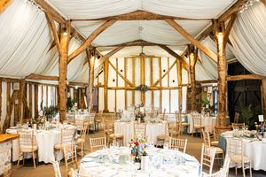 Rustic wedding barn reception venue with white draping, fairy lights and round guest tables.