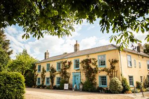 Charming yellow country house wedding venue with blue windows and climbing roses on gravel drive.