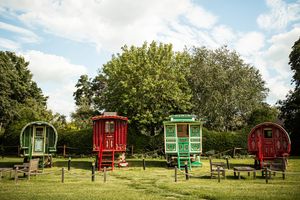 Four colorful vintage gypsy caravans on green lawn under blue sky at rustic wedding venue.