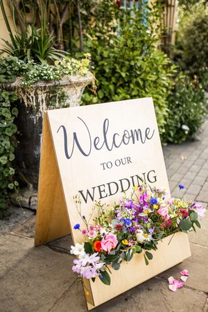 Wooden welcome to our wedding sign decorated with colorful wildflowers in garden setting.