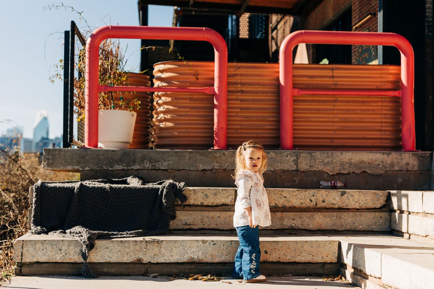 A young girl stands in Camp North End in front of a plant stand with the city in the background.