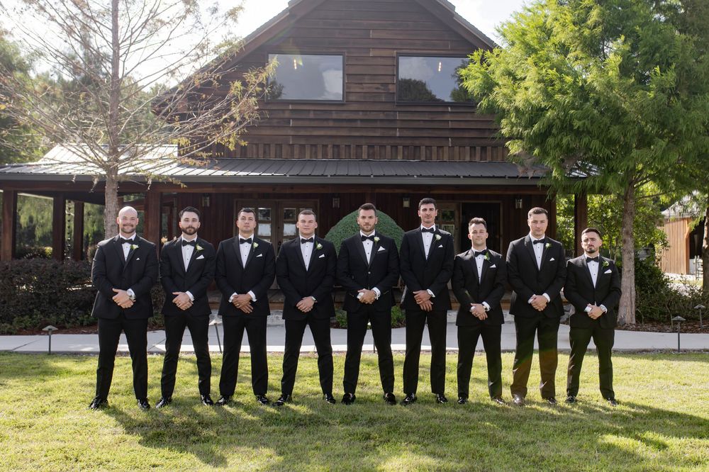 Wedding party members pose outdoors in formal attire against a landscaped backdrop.