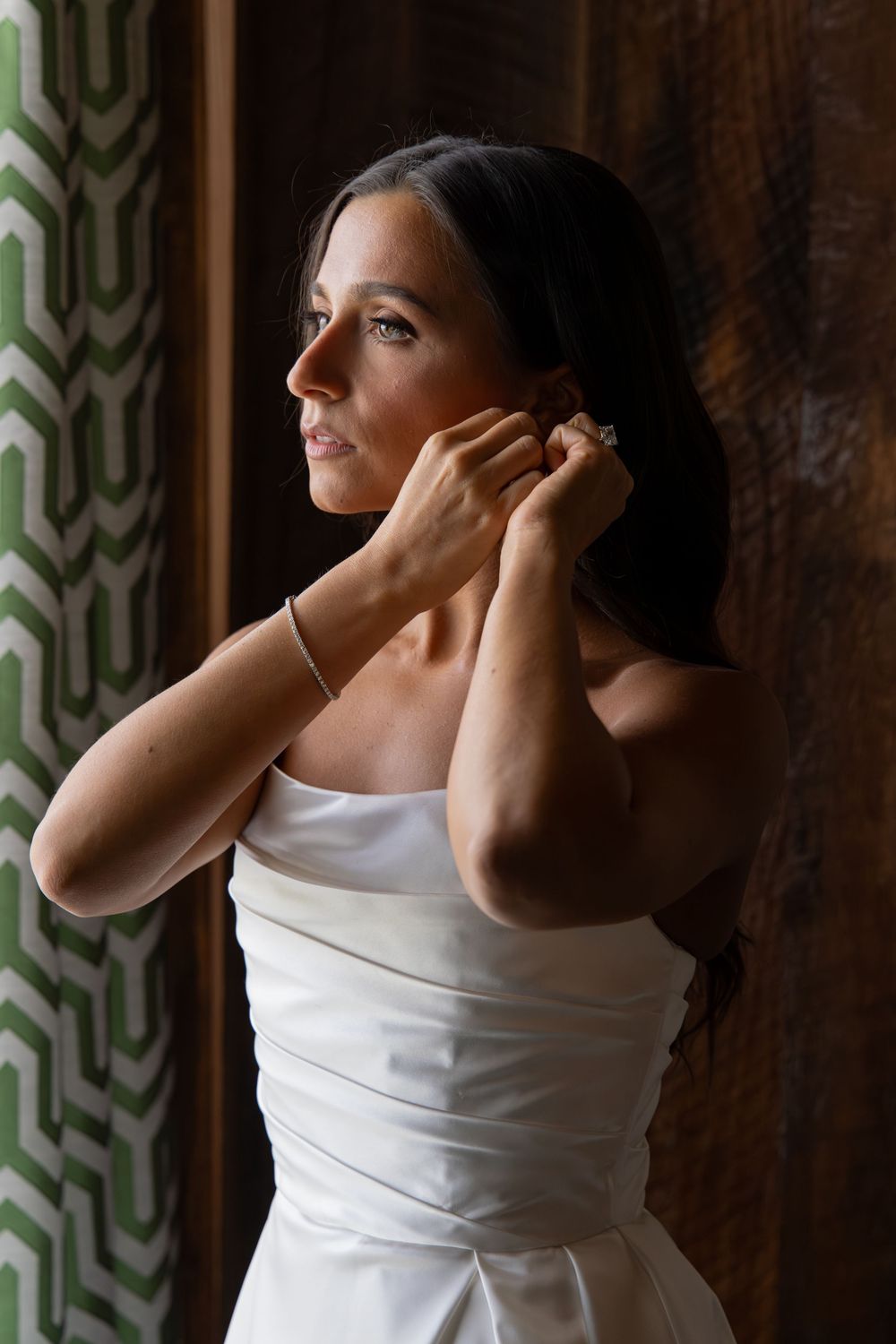A bride in a white dress puts on earrings while getting ready for her wedding.