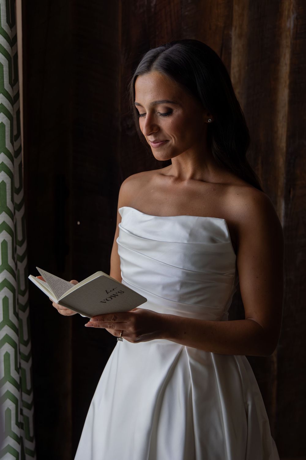 Bride in white strapless gown reading a letter in soft window light.
