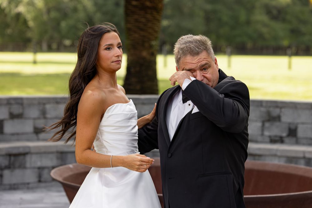A couple shares an intimate dance moment at an outdoor wedding reception with palm trees in the background.