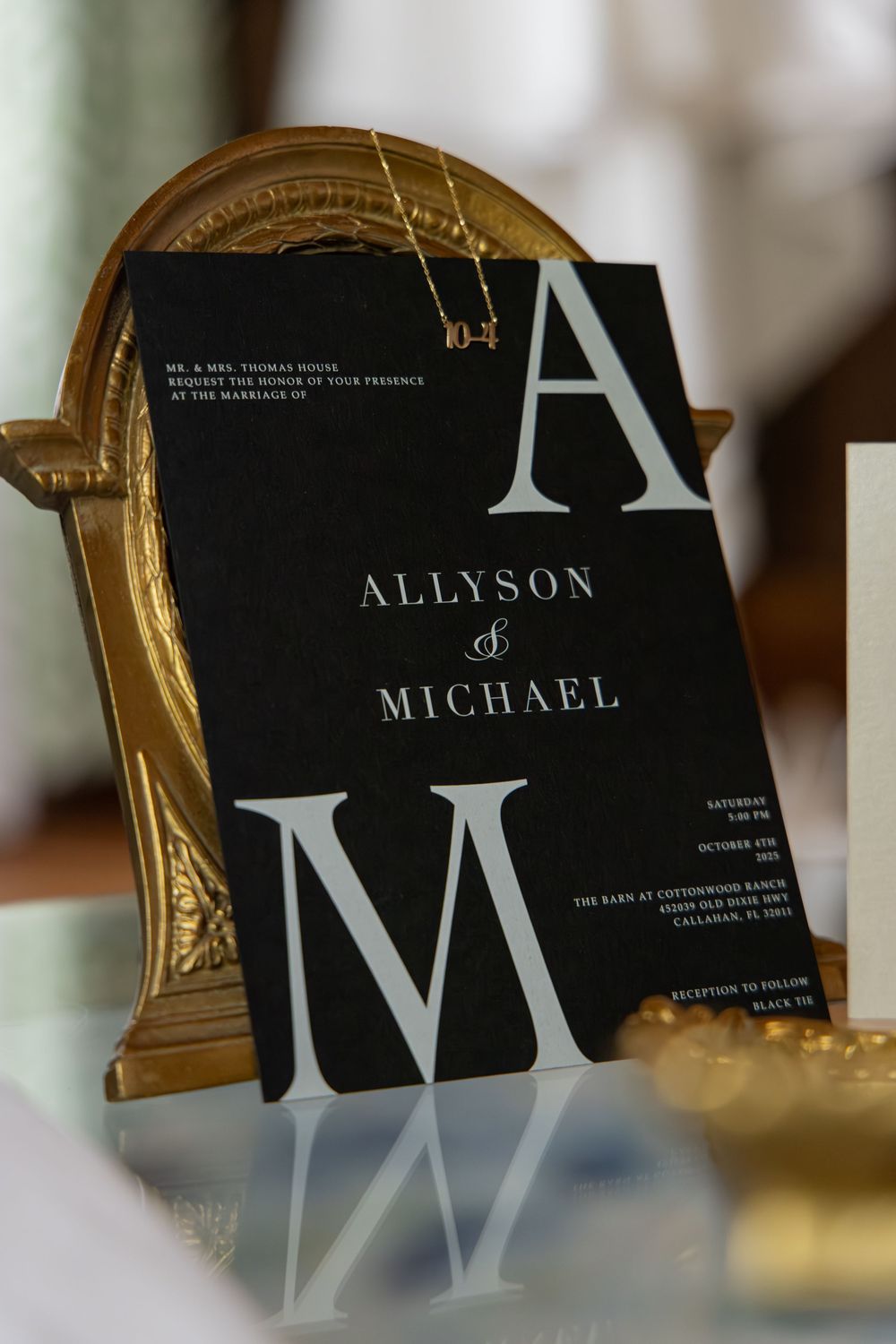 Elegant black and white wedding invitations with modern typography displayed against a gold frame.