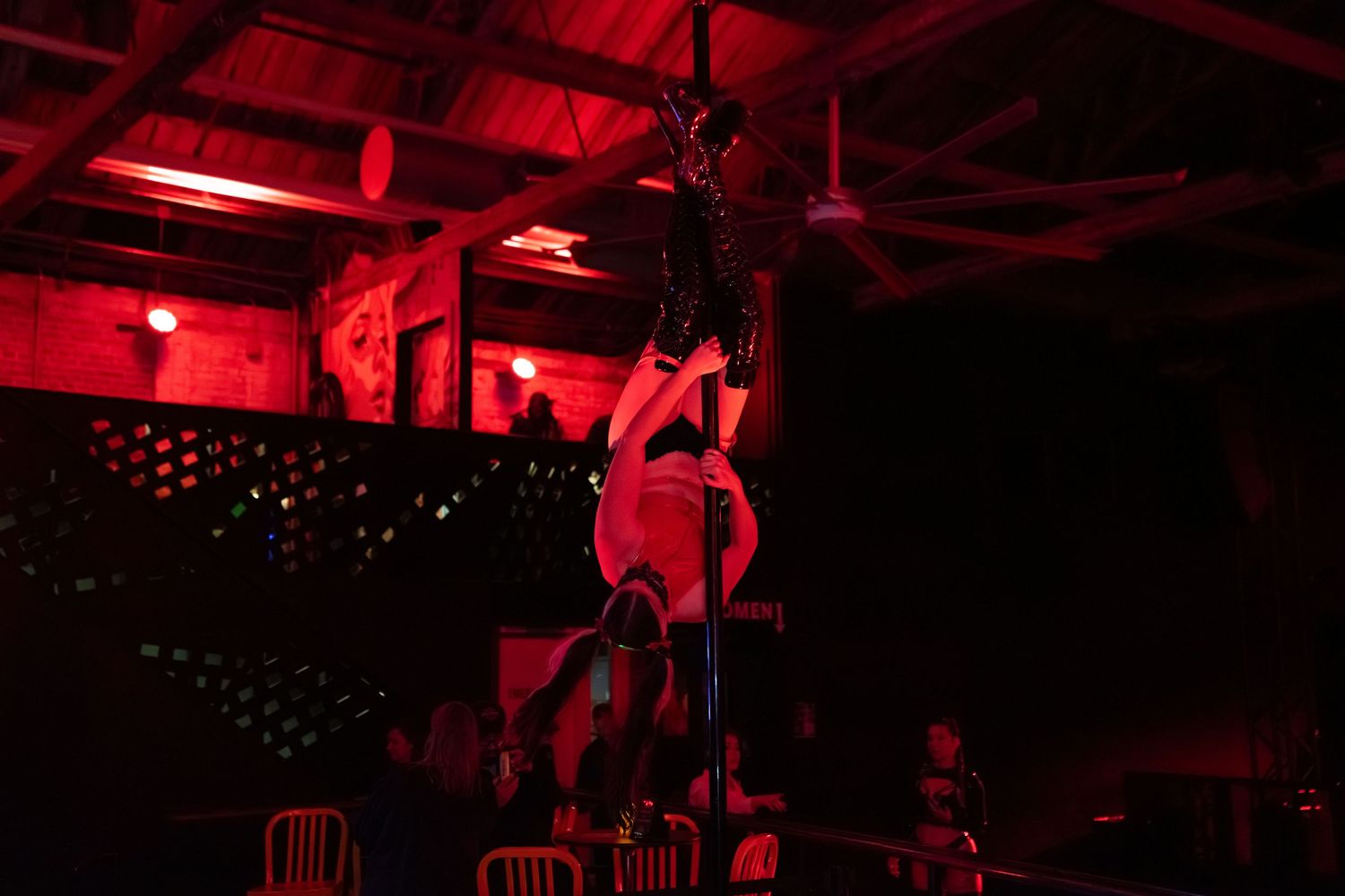 Atmospheric red lighting illuminates a dark nightclub interior with industrial-style ceiling and fixtures.