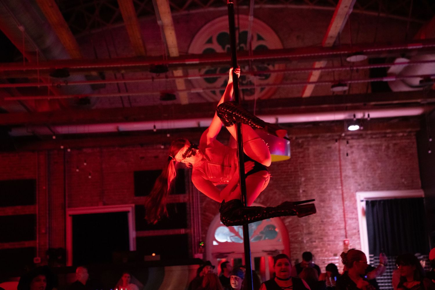 Aerial performer in red costume suspended from ceiling during dramatic performance with red lighting.