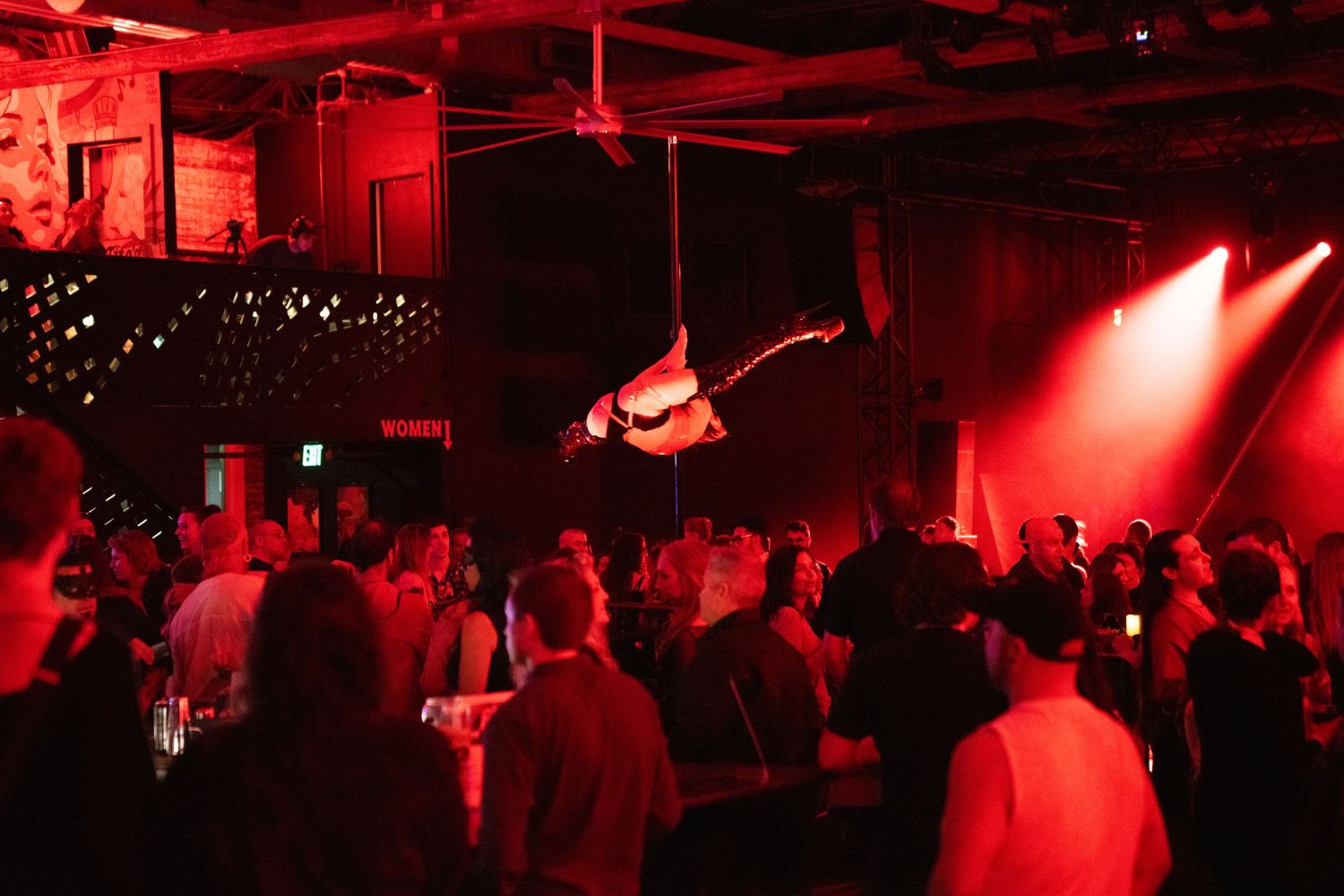 Crowded nightclub venue bathed in dramatic red lighting with silhouettes of people dancing.