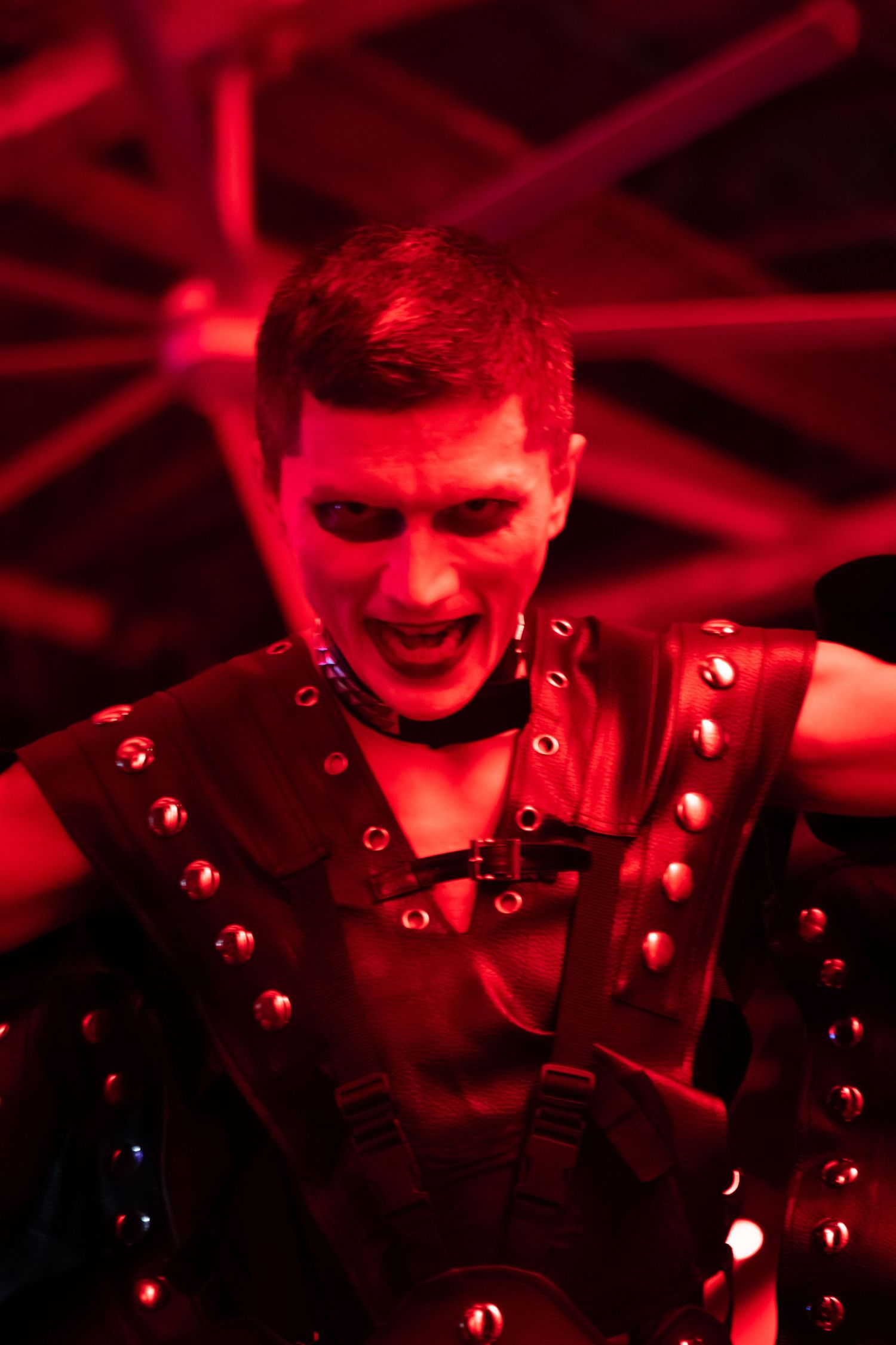 Performer in studded leather costume illuminated by intense red stage lighting during show.