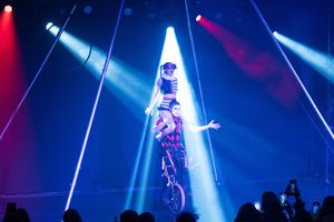 Aerial acrobat performing under dramatic blue and red spotlights in theatrical venue.