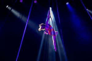 Two performers create dramatic silhouettes under bright stage lighting with deep blue atmospheric effects.