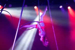 A pole dancer performs an athletic pose under dramatic purple and red stage lighting at a nightclub.