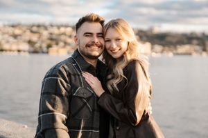 A couple shares intimate moments along a waterfront during a romantic photoshoot at sunset.