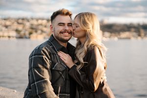 Couple sharing a romantic moment on a waterfront overlook with city views in the background.