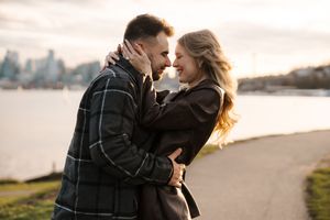 Romantic moment between couple on waterfront path with city skyline in background at dusk.
