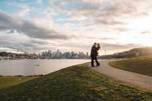Scenic panoramic view of a city skyline across the water during golden hour with people on a grassy hill.
