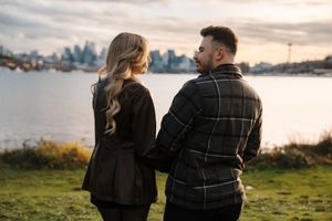 A couple sits together on a bench overlooking a scenic waterfront view during sunset.