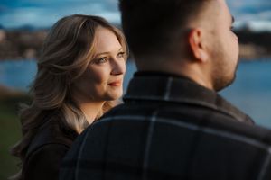 Romantic couple in silhouette stand close together against a waterfront backdrop at sunset.