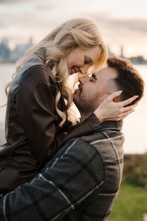 A romantic couple embraces and kisses outdoors during sunset in a scenic natural setting.