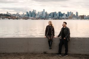 People enjoying the waterfront view of downtown Seattle from Alki Beach during golden hour.