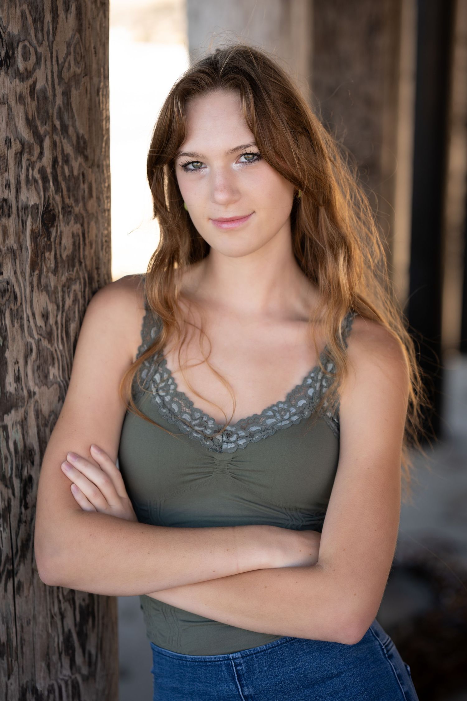 Woman in olive green tank top and jeans poses against rustic wooden post in casual portrait series.