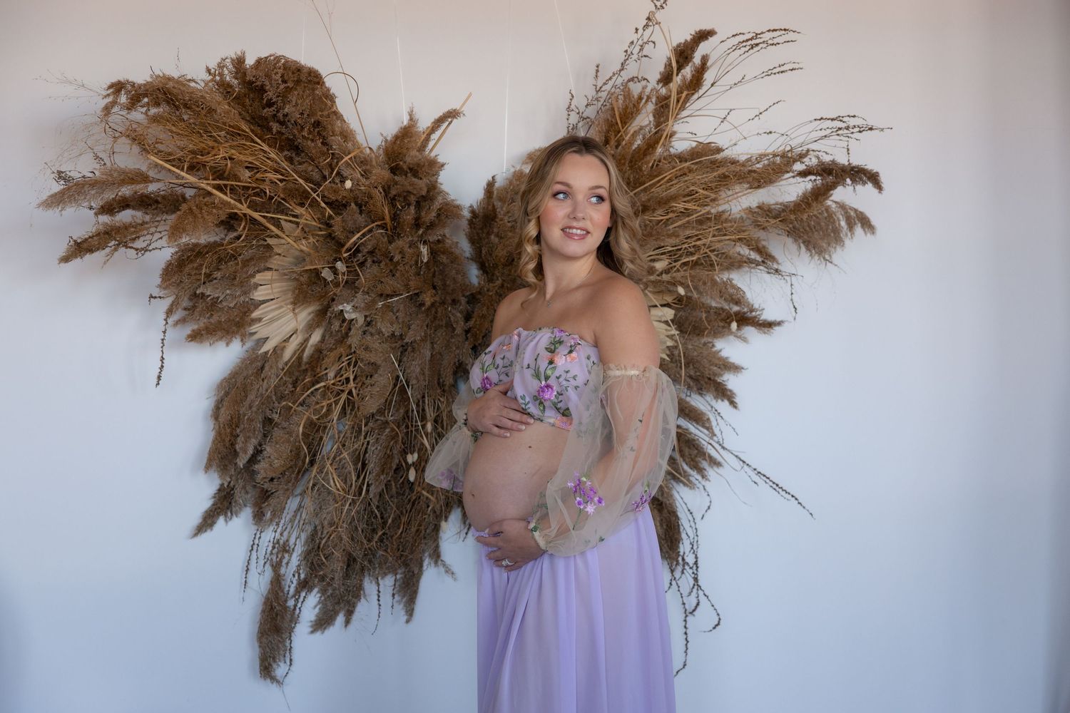 Dramatic maternity portraits with dried pampas grass arrangements against white backdrop.