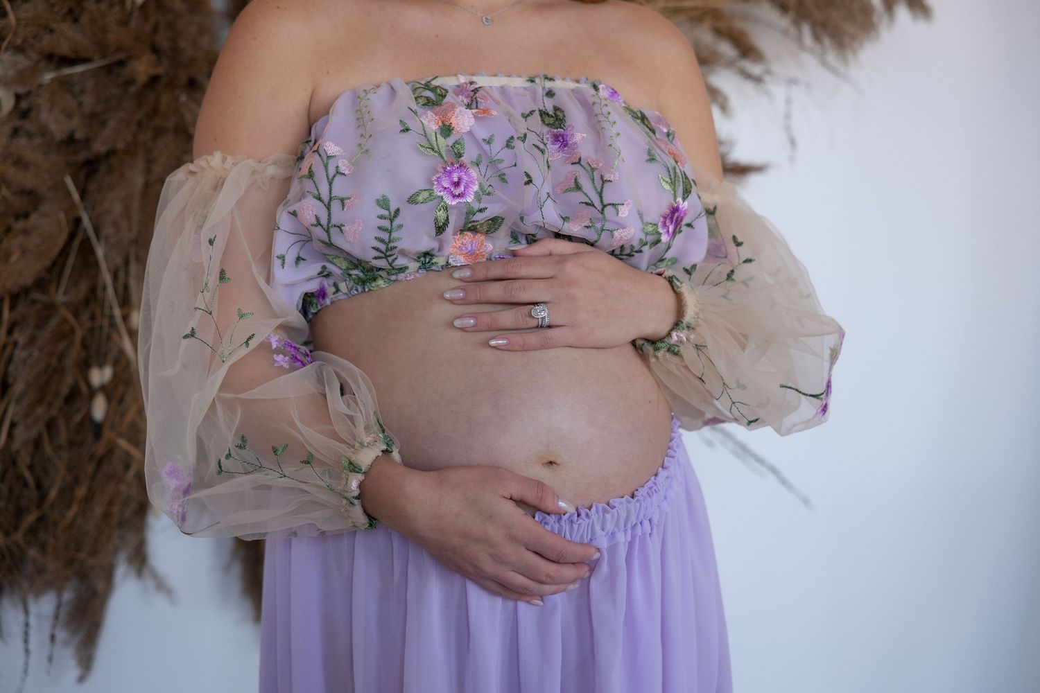 Ethereal maternity photos in flowing purple dress with floral details and pampas grass decor.