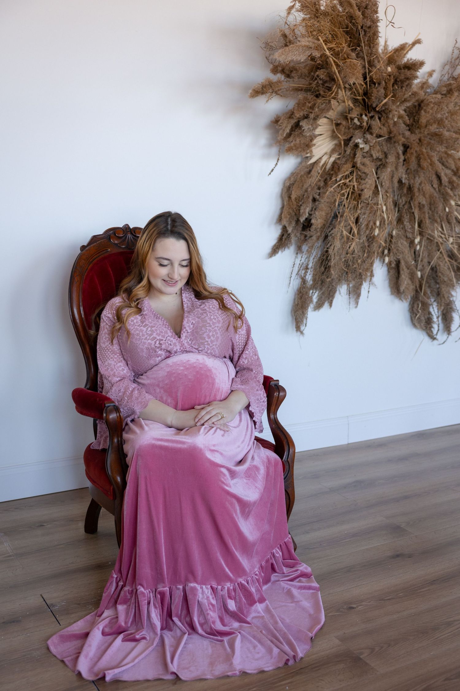 Maternity portrait with dried pampas grass decor and vintage chair in pink velvet dress.