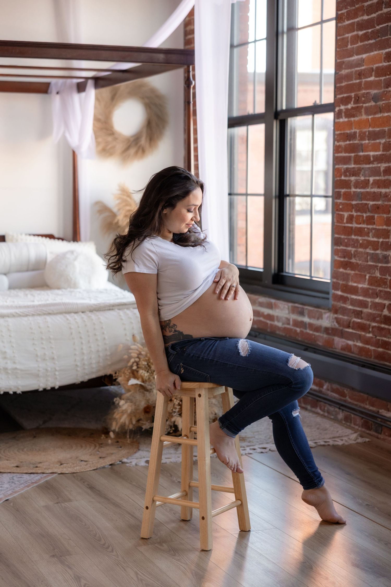 Artistic maternity portraits taken by a window in an industrial loft space.