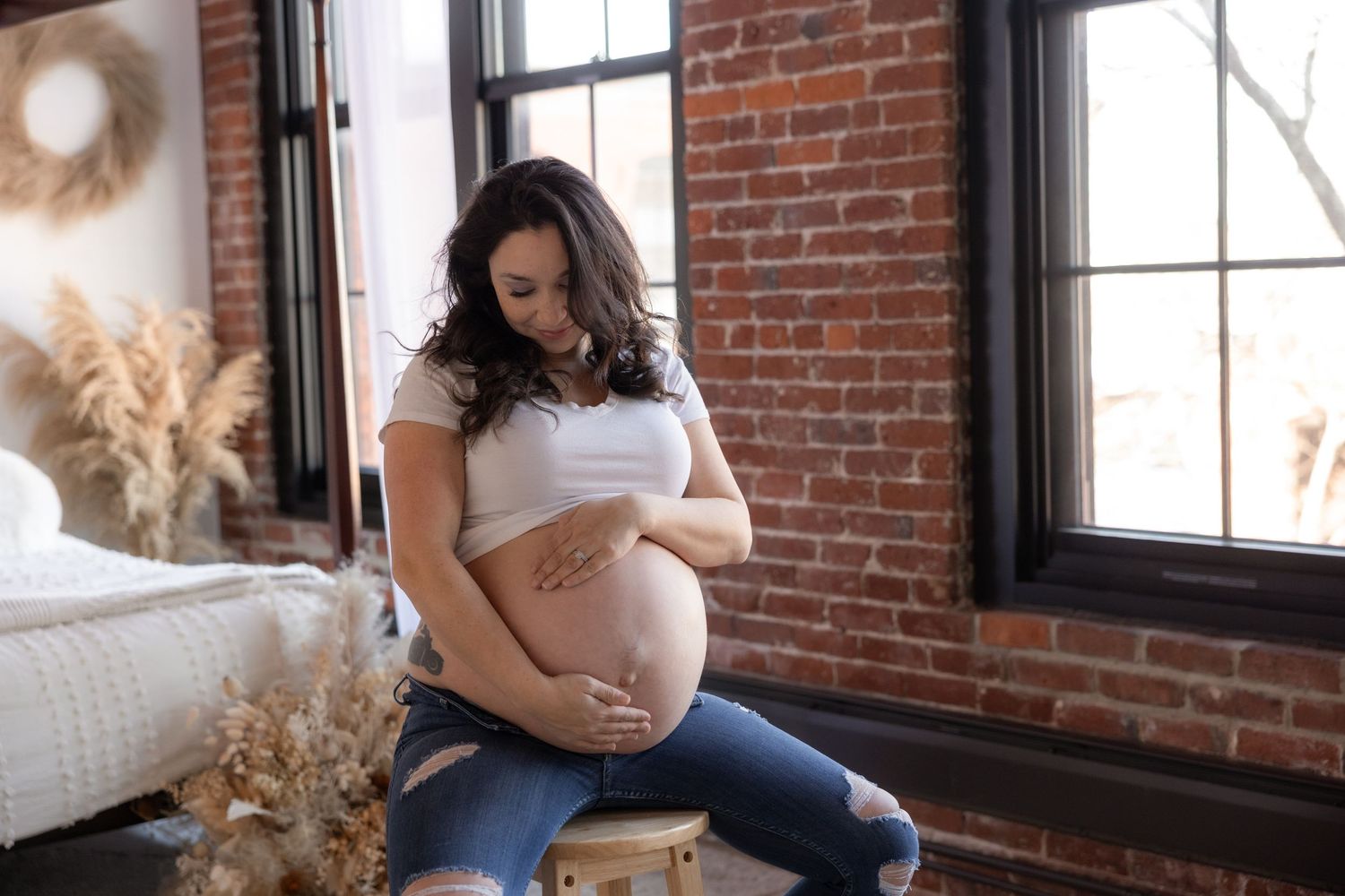 Natural light maternity session featuring casual poses against brick wall backdrop.