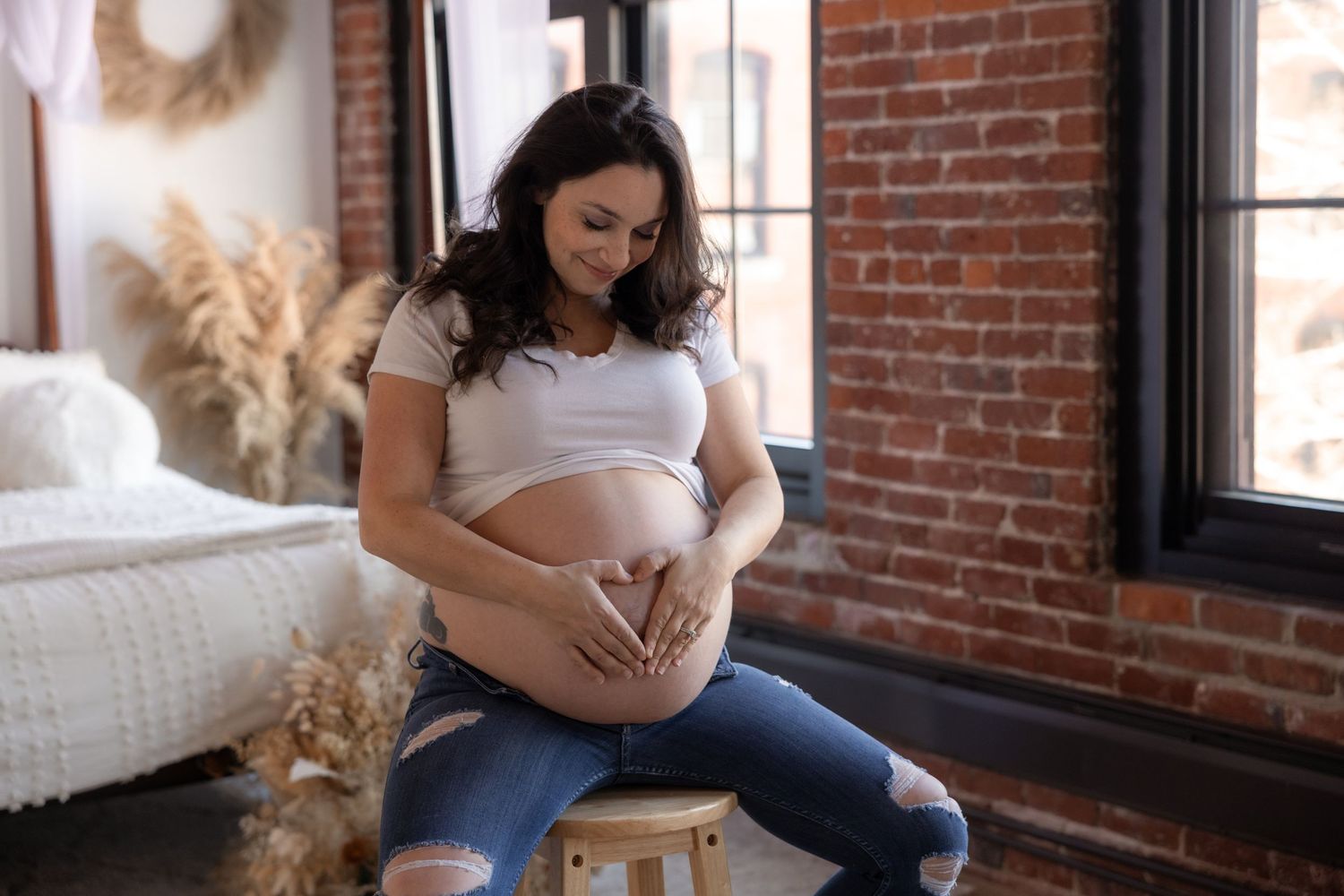 Candid maternity photos captured in a sunlit room with exposed brick walls.