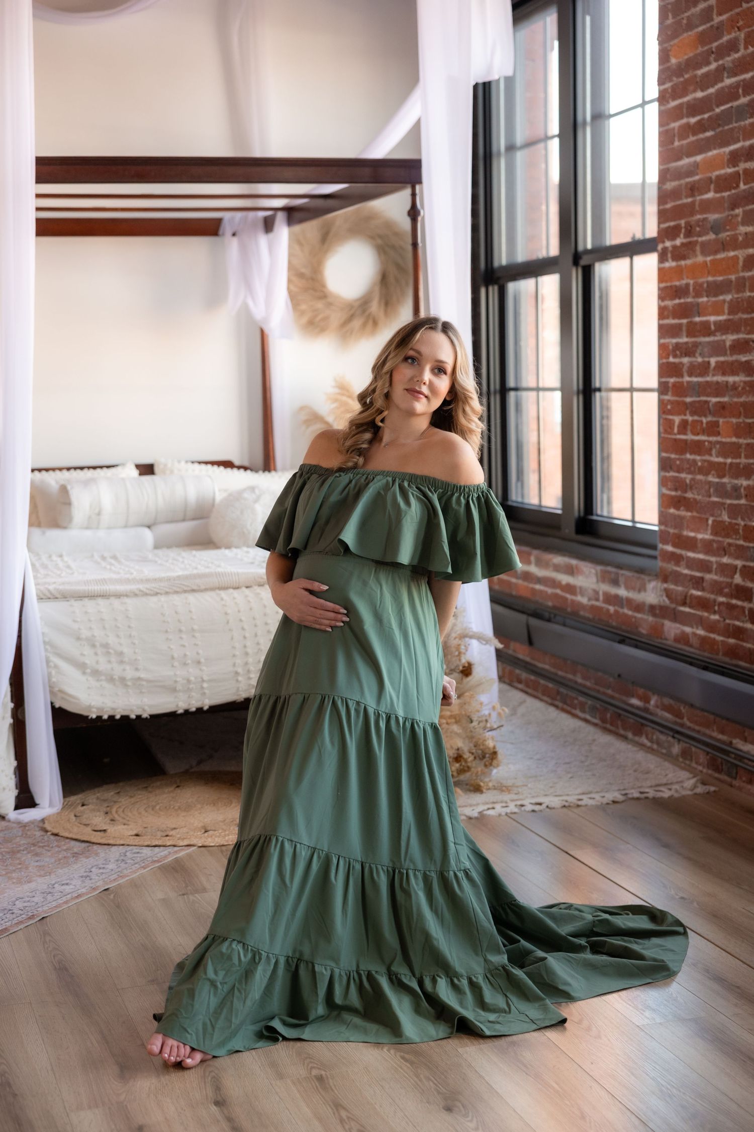 Figure in olive green off-shoulder dress poses gracefully in industrial brick loft space.