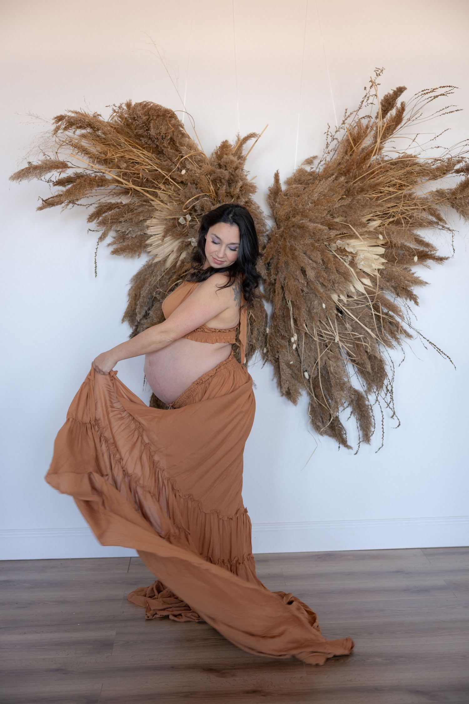 Artistic maternity photos with flowing brown fabric and dried pampas grass decorations.