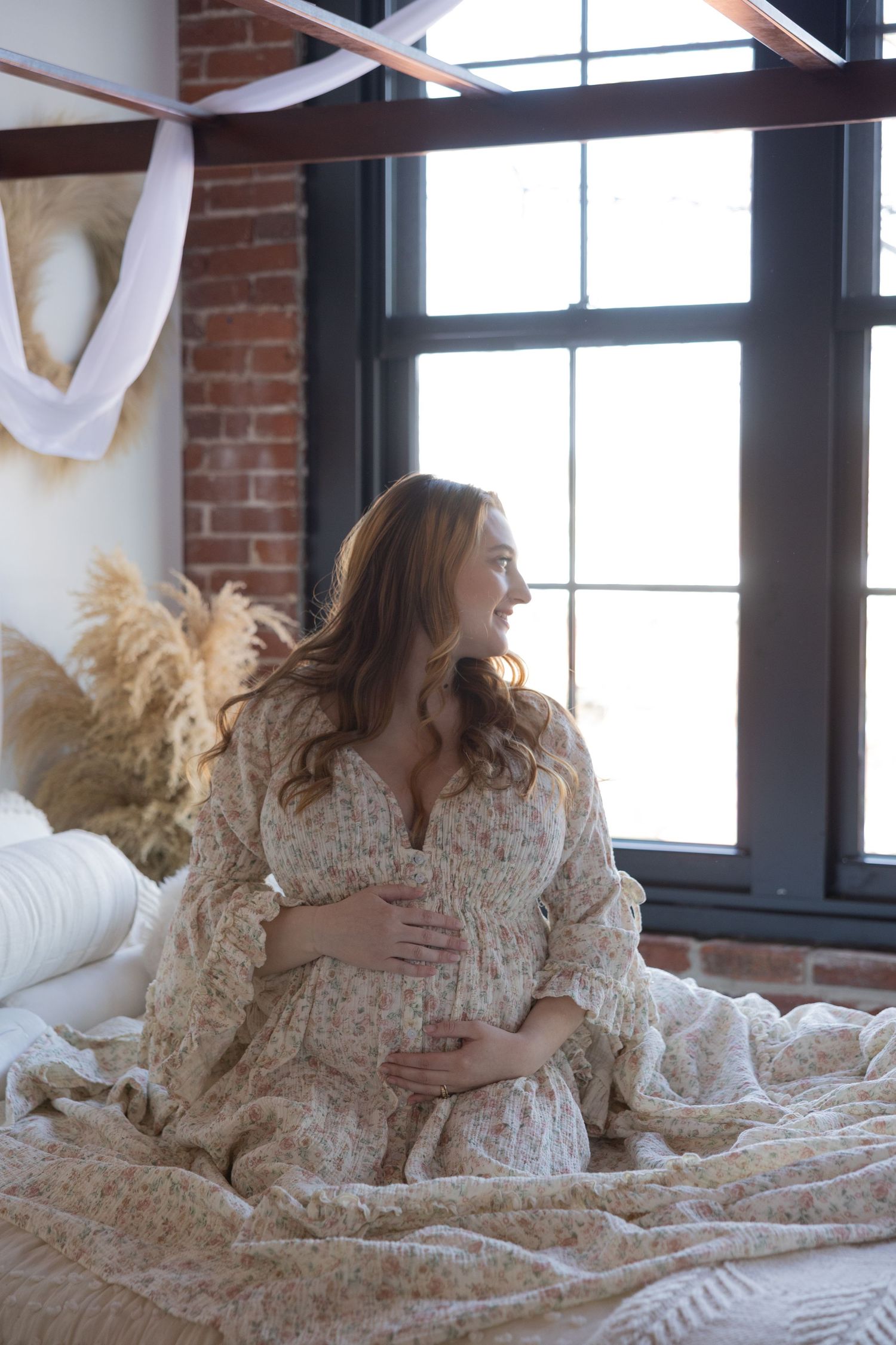 Ethereal maternity session with lace dress and natural window light in brick studio.
