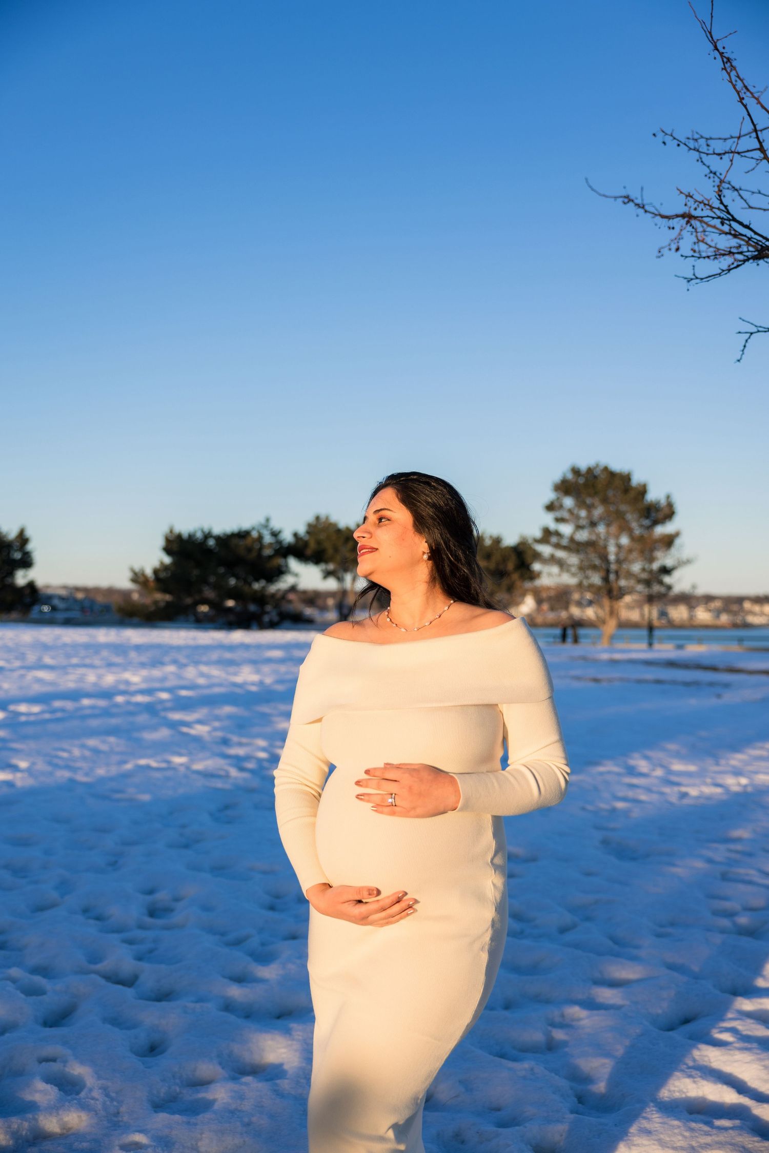 A person in white clothing stands in a snowy winter landscape with bare trees against a blue sky.