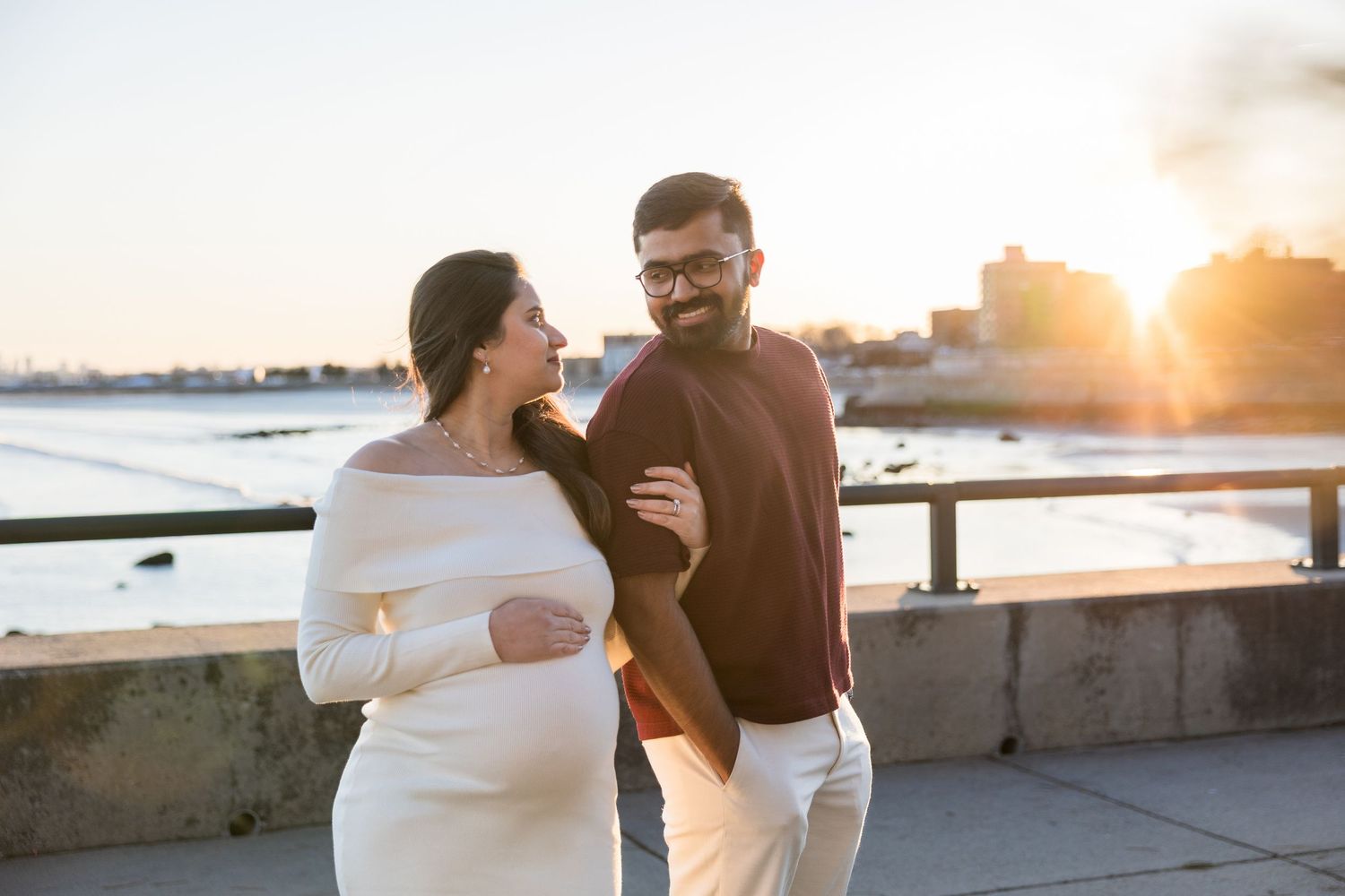 A couple embraces on a beach boardwalk during golden hour sunset creating a romantic silhouette against the ocean.