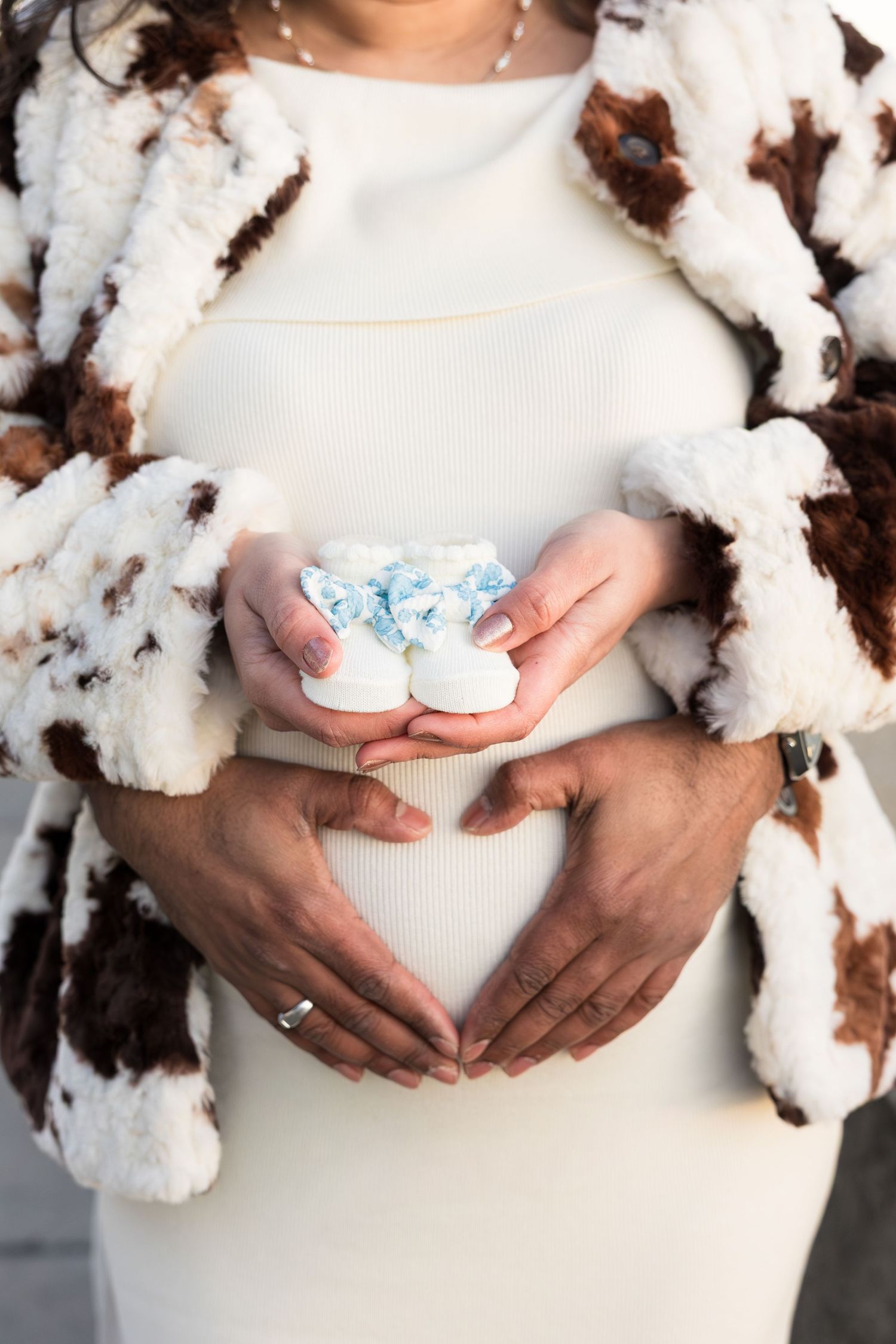 A pregnancy maternity photo series showing hands cradling a baby bump against white cotton flowers and fabric.