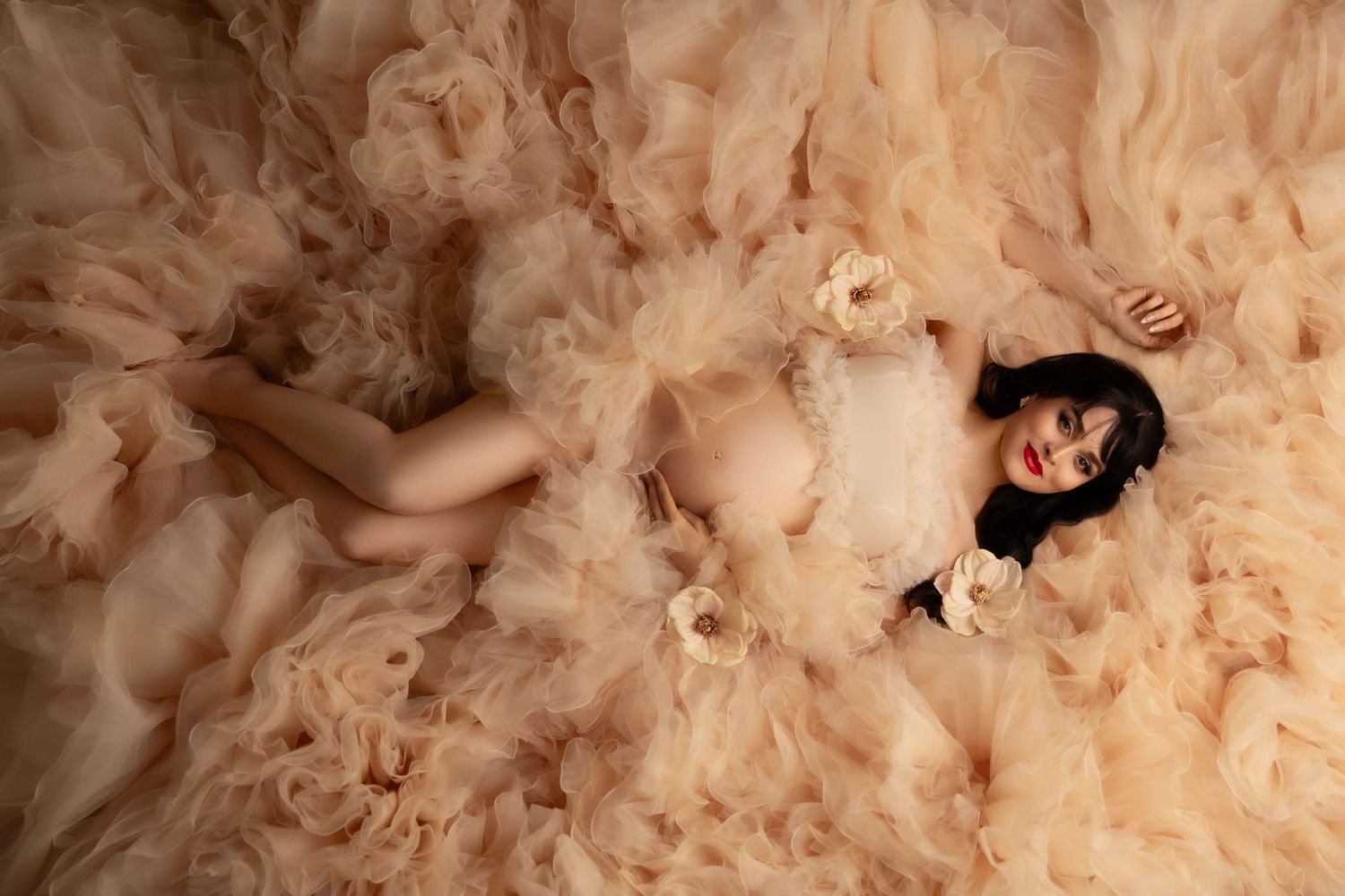 A figure lays surrounded by layers of flowing cream-colored tulle fabric in an ethereal fashion portrait.