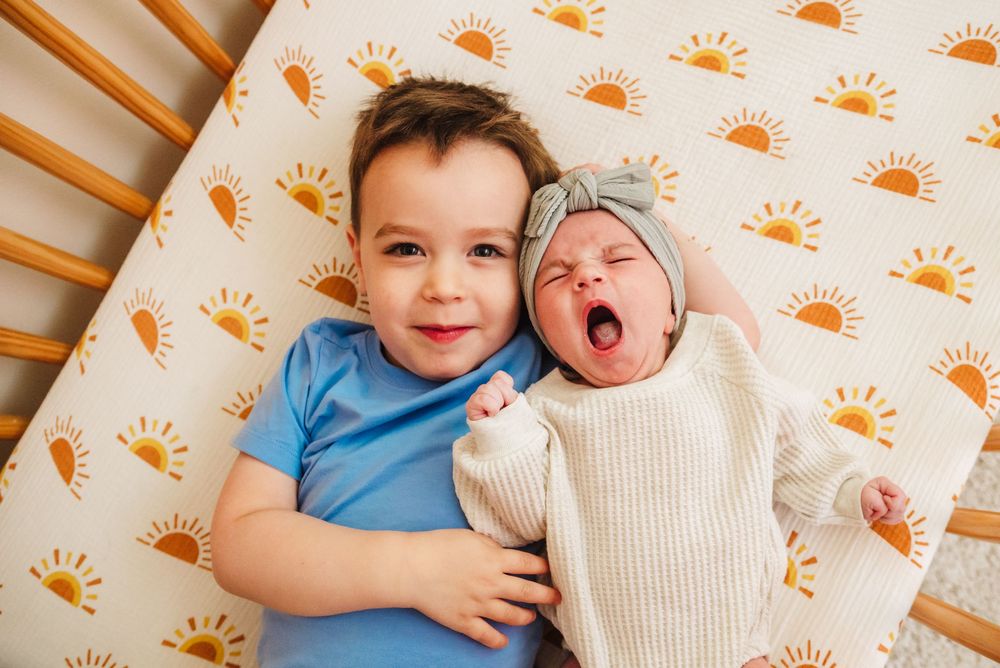 Siblings lying on orange sun-patterned wallpaper background share sweet moments together.