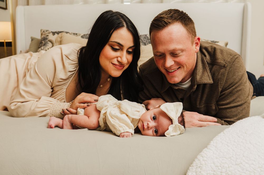 A loving family shares tender moments while lying together on a white bed in a cozy home setting.