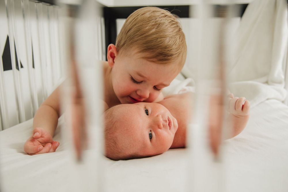 A series of four tender newborn baby photos showing close-up details through white crib slats.